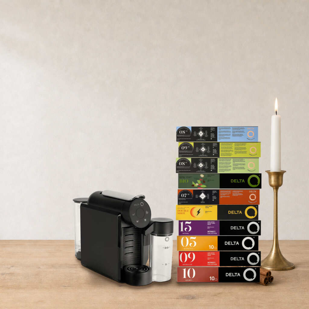 Coffret Cappuccino maison Delta Q sur une table en bois, près d’un bougeoir en laiton et de bâtons de cannelle
