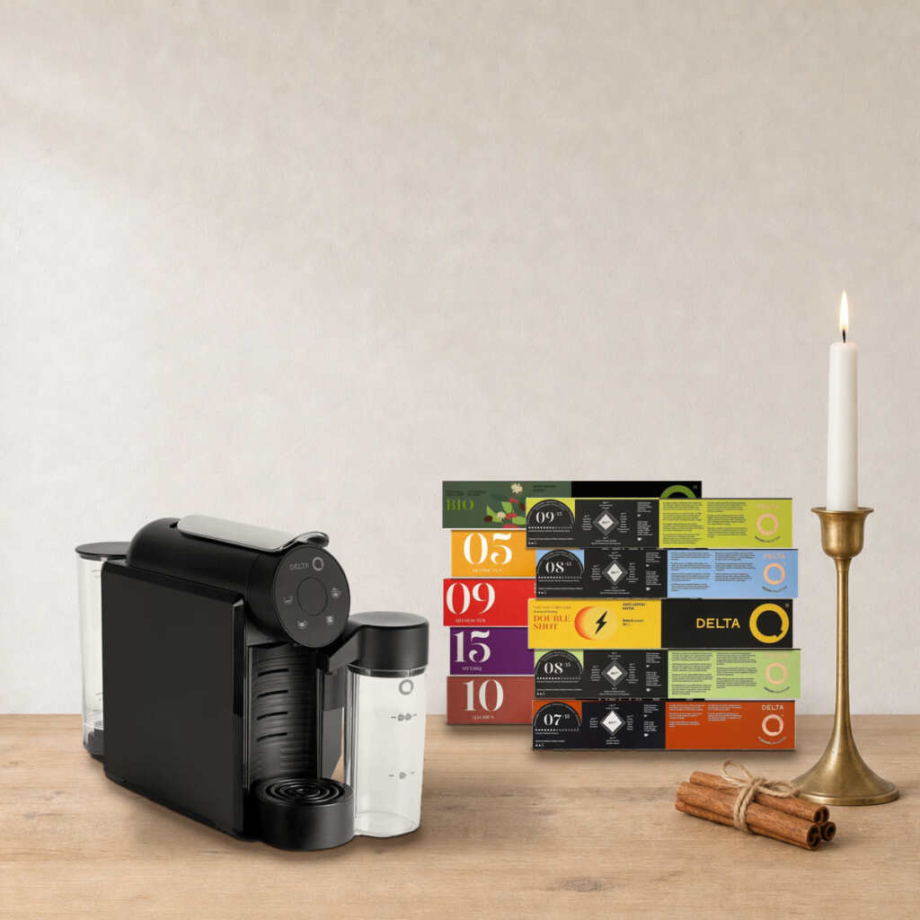 Coffret Cappuccino maison Delta Q sur une table en bois, près d’un bougeoir en laiton et de bâtons de cannelle