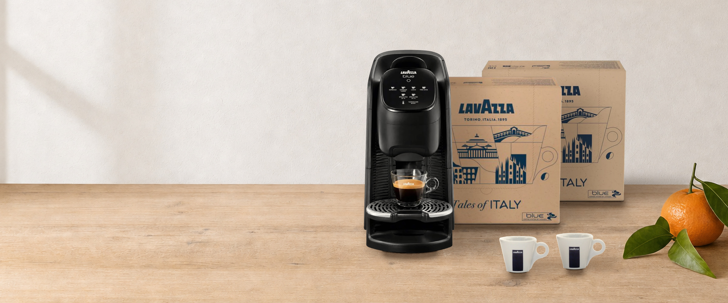 Coffret machine + cafés Lavazza Blue Classy Soul sur une table en bois, près d’une guirlande lumineuse et de clémentines