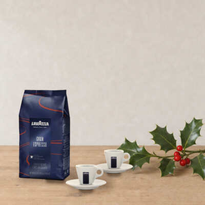 Set Espresso Lavazza sur une table en bois, près d’une branche de houx
